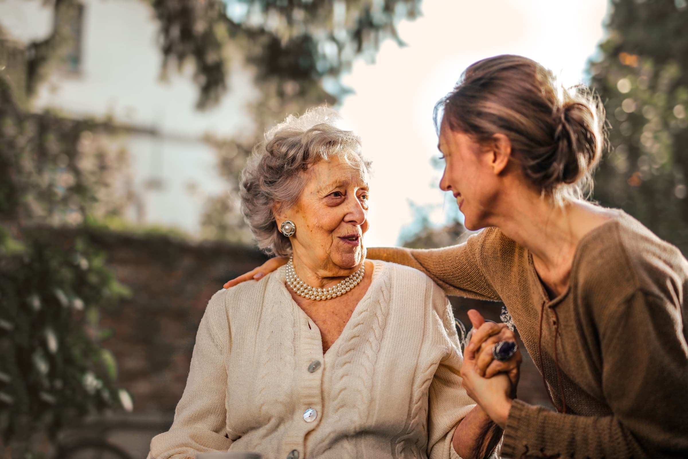 An adult daughter and her mother laughing together in a garden, golden afternoon light